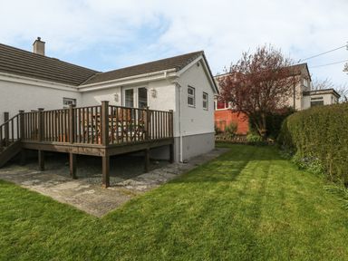 A wooden deck with chairs and table attached to a white house with lawn and trees at Tyn Y Giat in Brynsiencyn near Beaumaris