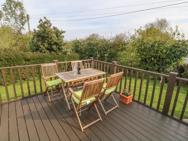 A wooden deck with table and chairs next to a garden with shrubs at Tyn Y Giat in Brynsiencyn near Beaumaris