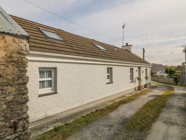 Exterior view of a white single-story house with a tiled roof and skylights along a gravel driveway at Tyn Y Giat Brynsiencyn near Beaumaris