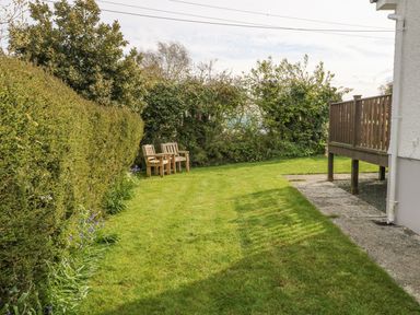 A garden with wooden benches trees and a lawn next to a house with a raised wooden deck at Tyn Y Giat in Brynsiencyn near Beaumaris