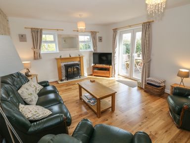 A living room with green leather sofas a fireplace a wooden coffee table a television and glass doors leading outside at Tyn Y Giat in Brynsiencyn near Beaumaris