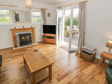 A living room with a wooden coffee table a fireplace and a television near open double doors leading to an outdoor patio at Tyn Y Giat in Brynsiencyn near Beaumaris