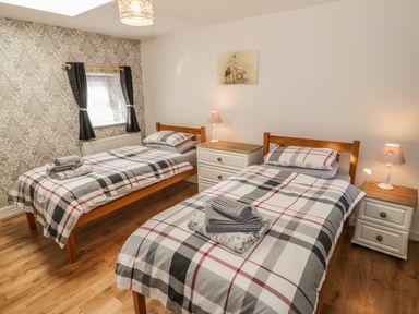 A bedroom with two single beds with plaid bedding wooden floors and bedside tables with lamps at Tyn Y Giat in Brynsiencyn near Beaumaris