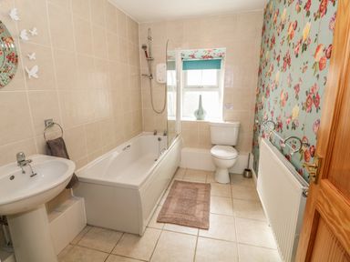 A bathroom with a bathtub sink toilet and floral wallpaper at Tyn Y Giat Brynsiencyn near Beaumaris