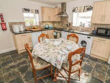 A kitchen with wooden cabinets black countertops a round table with a tablecloth and four chairs at Tyn Y Giat Brynsiencyn near Beaumaris