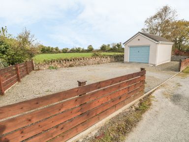 A gravel driveway with wooden fencing leading to a small detached garage with a blue door in a rural setting at Tyn Y Giat Brynsiencyn near Beaumaris