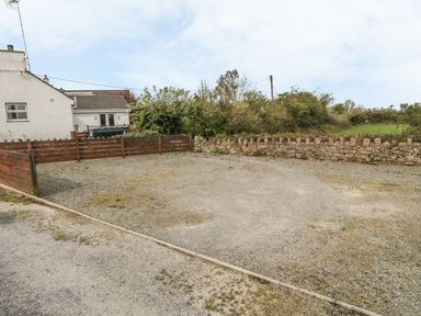 An outdoor gravel area with a wooden fence and a stone wall next to a white building at Tyn Y Giat in Brynsiencyn near Beaumaris