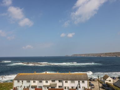A row of houses by the ocean with waves and a cliff in the background at Sennen Heights in Sennen Cove near Penzance