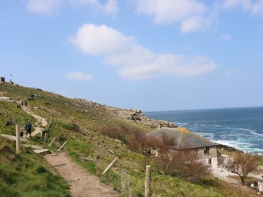 A coastal path with people walking dogs near a stone building by the ocean at Sennen Heights in Sennen Cove near Penzance