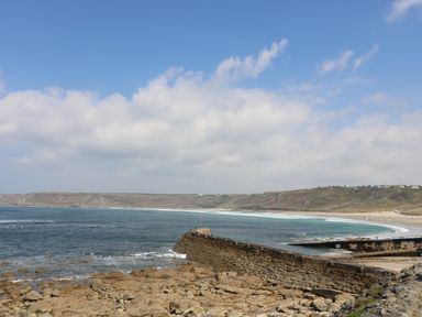 A rocky shoreline with a stone pier extending into the sea and a sandy beach in the background at Sennen Heights Sennen Cove near Penzance