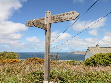 A wooden signpost with directions near a coast showing public footpaths and byways with ocean and houses in the background at Sennen Heights Sennen Cove near Penzance