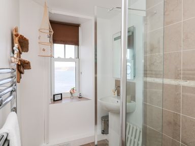 A bathroom with a shower enclosure sink mirror window with a brown blind and towel rail at Sennen Heights in Sennen Cove near Penzance