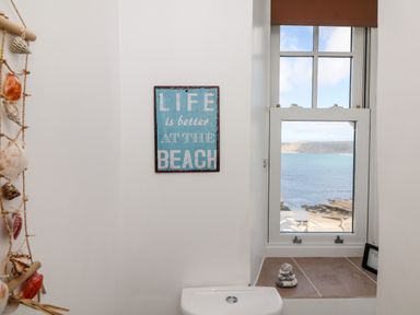 A bathroom window overlooking the sea with shells hanging on the wall and a sign saying life is better at the beach at Sennen Heights in Sennen Cove near Penzance