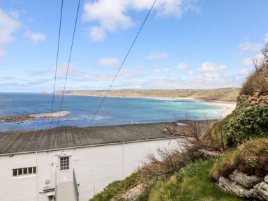 A coastal view with a white building roof in the foreground and a sandy beach with cliffs in the background at Sennen Heights in Sennen Cove near Penzance