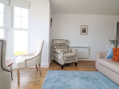 A living room with beige and plaid chairs a blue rug wooden floor and a sofa with cushions at Sennen Heights in Sennen Cove near Penzance