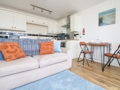 A kitchen and dining area with a beige sofa and orange cushions at Sennen Heights in Sennen Cove near Penzance