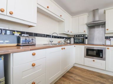 A kitchen with white cabinets wooden knobs a wooden countertop a toaster a bread box a kettle a microwave an oven and a stainless steel range hood at Sennen Heights in Sennen Cove near Penzance