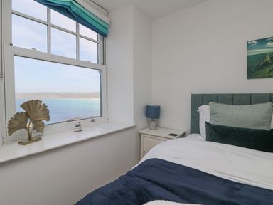 A bedroom with a bed next to a window showing a sea view at Sennen Heights in Sennen Cove near Penzance