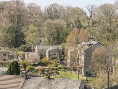Stone houses surrounded by trees and gardens with a stone wall and lawns at Doe Foot Cottage in Ingleton