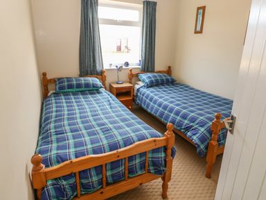 A small bedroom with two single beds covered with blue plaid bedding a wooden nightstand with a lamp between them at Surf in Hunstanton