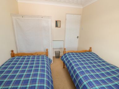 A bedroom with two single beds with blue plaid bedspreads a covered window a small wall mirror and a white door at Surf in Hunstanton