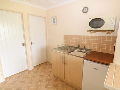 A kitchen area with a sink, dish rack, microwave, fridge, and two closed doors at Surf in Hunstanton