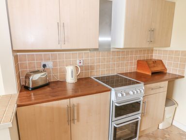 A kitchen with wooden cabinets a stove a toaster a kettle and a bread box at Surf Hunstanton