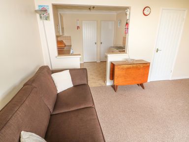A brown sofa with white pillows next to a wooden drop leaf table and a kitchen area in the background at Surf in Hunstanton