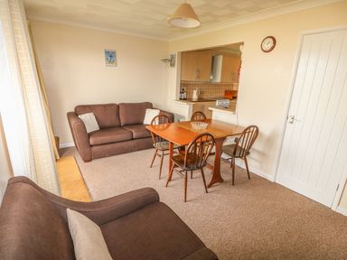 A dining area with a wooden table and four chairs next to a living room with two brown sofas and a kitchen in the background at Surf Hunstanton