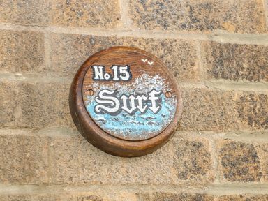 A round wooden sign with number 15 and word Surf attached to a stone wall at Surf in Hunstanton