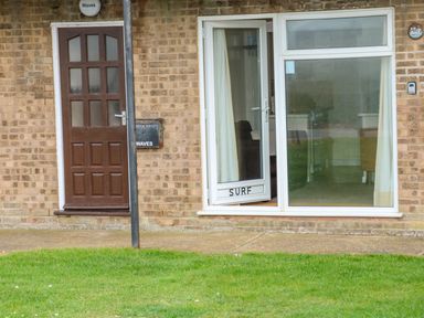 A brick exterior of a building with a brown door and a white patio door labeled Surf at Surf in Hunstanton