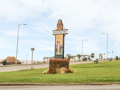 A town sign for Hunstanton on a grassy area near a road with streetlights and benches at Surf Hunstanton
