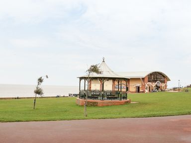 A grassy park area with a gazebo and a building near the waterfront at Surf in Hunstanton