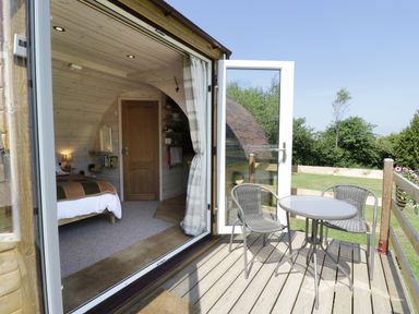 A small wooden deck with table and chairs outside a pod with an open door showing a bedroom inside at Idris Pod in St Asaph