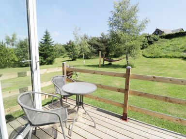 A small outdoor deck with two chairs and a round table overlooking a grassy yard with trees and a hammock at Idris Pod in St Asaph