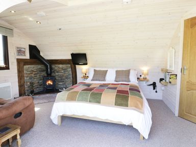A bedroom with a bed a fireplace a wall-mounted TV and a brown armchair at Idris Pod in St Asaph