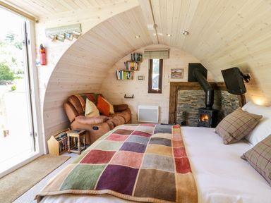 A bedroom with a bed covered by a patchwork blanket a brown leather sofa a small side table a wood burning stove and bookshelves at Idris Pod in St Asaph