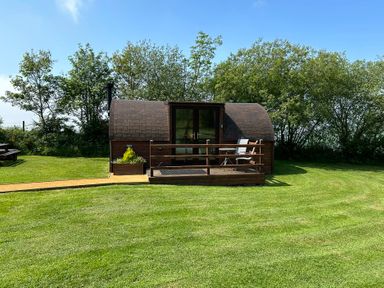 A cabin with a deck and chairs in a grassy area at Idris Pod in St Asaph