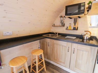 A small kitchen area with wooden stools a sink microwave kettle and cooking utensils at Gelert Pod in St Asaph