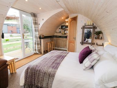 A bedroom with a bed and pillows next to a small kitchen and sliding glass door at Gelert Pod in St Asaph