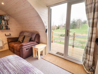 A brown leather armchair with side tables next to sliding glass doors showing a green garden outside at Gelert Pod in St Asaph