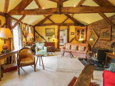 A living room with exposed wooden beams a fireplace and various chairs at Dolgenau Hir - The Barn in Llawr y Glyn near Trefeglwys