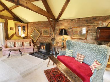A living room with two sofas a wood stove and wooden beams on the ceiling at Dolgenau Hir - The Barn in Llawr y Glyn near Trefeglwys