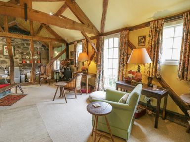 A living room with wooden beams rugs chairs tables and lamps at Dolgenau Hir - The Barn in Llawr y Glyn near Trefeglwys