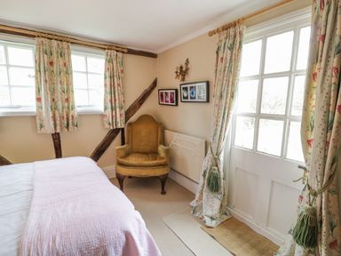 A bedroom with a bed, an armchair, framed pictures on the wall, and floral curtains at Dolgenau Hir - The Barn in Llawr y Glyn near Trefeglwys