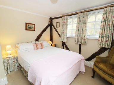 A bedroom with a double bed bedside tables windows with floral curtains and an armchair at Dolgenau Hir - The Barn in Llawr y Glyn near Trefeglwys