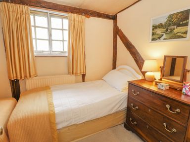 A small bedroom with a single bed beside a window and a wooden dresser with a lamp and mirror at Dolgenau Hir - The Barn Llawr y Glyn near Trefeglwys