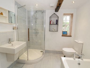 A bathroom with a corner shower, sink, toilet, and window at Dolgenau Hir - The Barn Llawr y Glyn near Trefeglwys