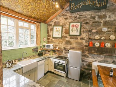 A kitchen with stone walls, green brick backsplash, appliances, knife rack, and wooden dining table at Dolgenau Hir - The Barn in Llawr y Glyn near Trefeglwys