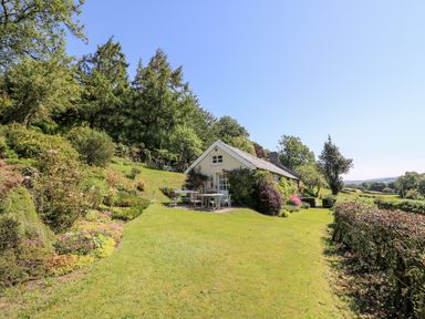 A small house with outdoor furniture on a lawn surrounded by trees and plants at Dolgenau Hir - The Barn in Llawr y Glyn near Trefeglwys